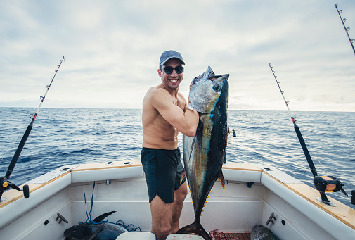 Man on a boat in the North Atlantic ocean holding his catch of large tuna fish and smiling.