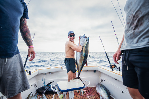 Man on a boat in the North Atlantic ocean holding his catch of large tuna fish and smiling.