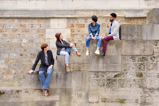 Diverse group of friends interacting, sitting on steps in Paris, France, Latin Quarter on spring day.