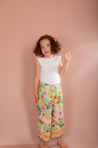Beautiful little girl, standing, redhead, posing for the camera. Isolated on salmon background.