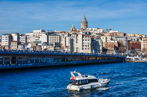 Istanbul, Turkey : Jan 09, 2023: Boat sailing in Bosphorus Strait, with Istanbul skyline in the background, overlooking Galata Bridge with traditional fish restaurants and Galata Tower, Istanbul, Turkey