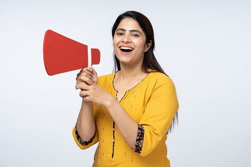Portrait of young woman screaming in megaphone, announcing important information on white background