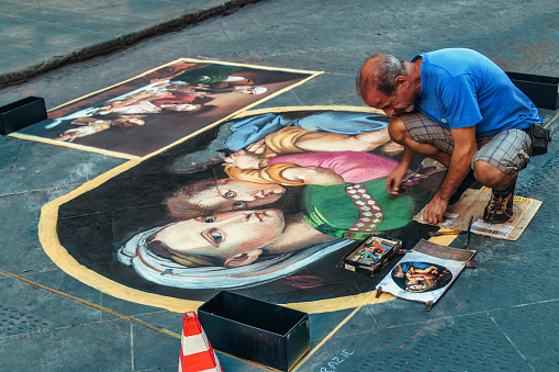 Florence, Italy - August 13, 2016: Pavement artists painting Madonna della Seggiola or Madonna della Sedia with chalk and pastels on the street of Florence, Italy