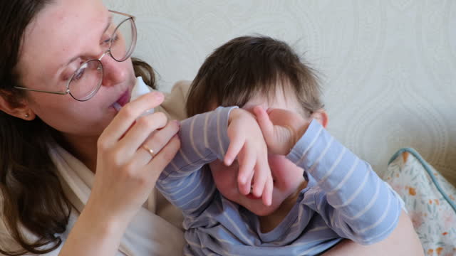 A mother woman sucks a runny nose from a baby with a snot pump. Mom cleans child's nose with a snot pump Kid aged about two years (one year nine months)