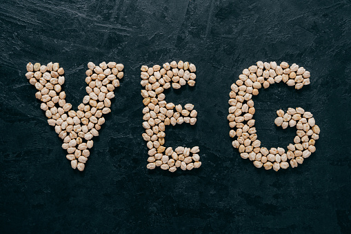 Uncooked chickpeas shaped in letters veg, isolated over dark background. Vegetarianism and healthy eating concept. Healthy nutrition