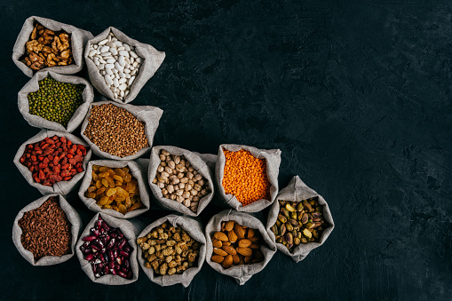 Horizontal shot of little sacks filled with almonds, walnuts, raisins, garbanzo, kidney bean, red goji, isolated over dark background, blank space for your advert