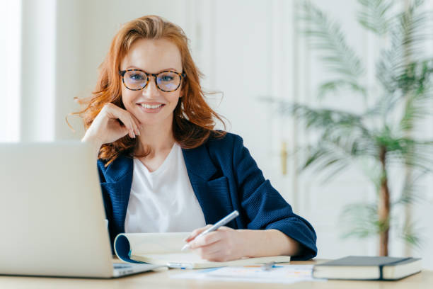 istock Happy successful female writes checklist in notepad, works on creative ideas for startup project, searches necessary information on laptop computer, poses at coworking space, works freelance 1483074469