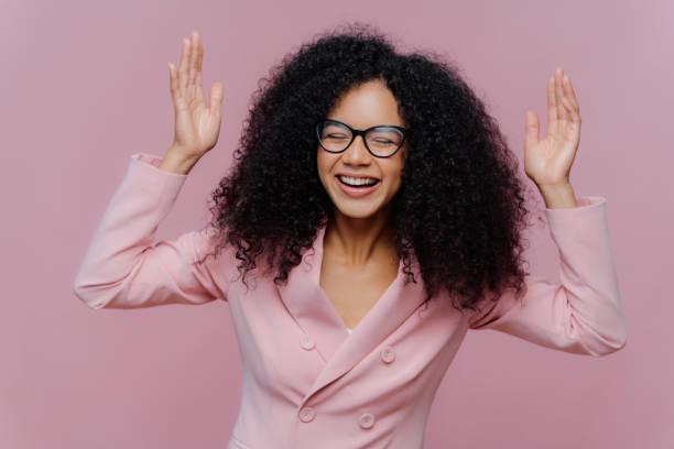 istock Overjoyed emotional female entrepreneur raises hands, laughs sincerely, wears spectacles and formal jacket, works in business sphere, poses indoor against purple background. Happy emotions concept 1483076208