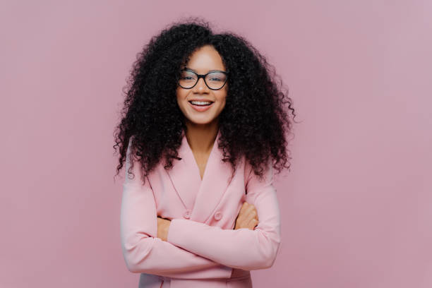 istock Pleased curly haired woman wears optical glasses for vision correction, elegant suit, keeps hands crossed over chest, poses against purple background, comes on job interview. Businesswoman at work 1483076212