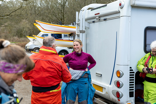 An over the shoulder side view of a group of sea kayakers who are unloading the van and getign the gear ready and all of the safety equipment ready. They are enjoying coastal weather on the coast of Dumfries in Scotland.