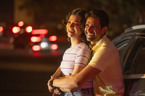 Smiling young couple leaning on car and admiring view outdoors at night