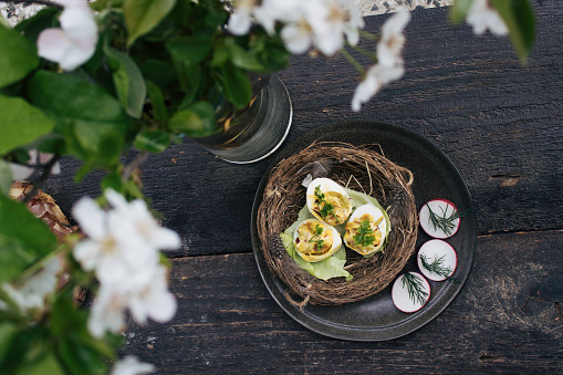 Easter plate decoration on kitchen table designed with flowers and food. Ham. eggs, tomato and more, are nicely placed in order on plate. Bird nest with boiled and seasoned eggs.