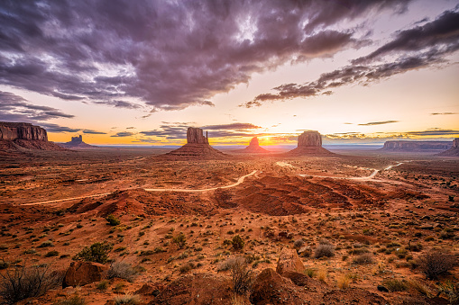 Wide angle overlook panoramic view of buttes and horizon in Monument Valley at sunrise colorful light and sunburst in Arizona with orange rocks