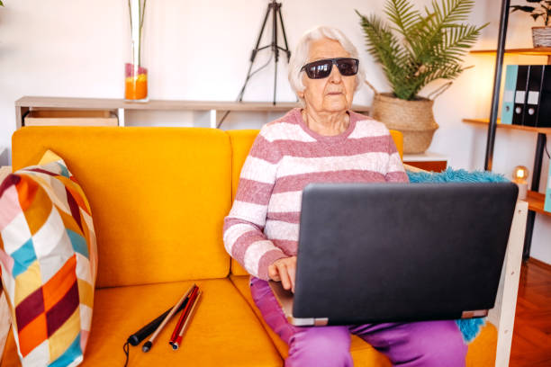 istock Blind old woman sitting on sofa in living room using laptop 1483084457