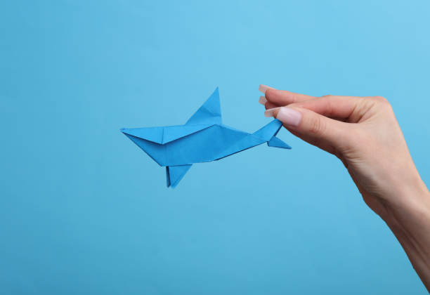 istock Female hand holds origami shark on blue background. Hobby, creativity 1483084559