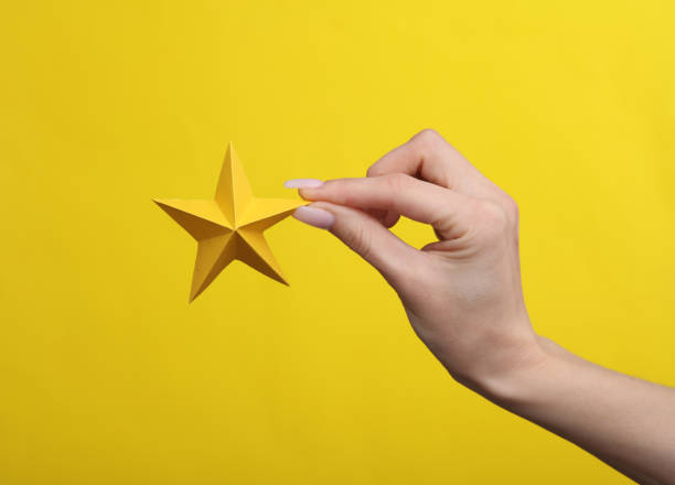 istock Woman's hand holding a paper star on a yellow background 1483084568