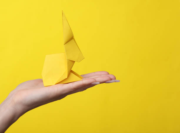 istock Female hand holds origami Rabbit on yellow background. Hobby, creativity 1483084572