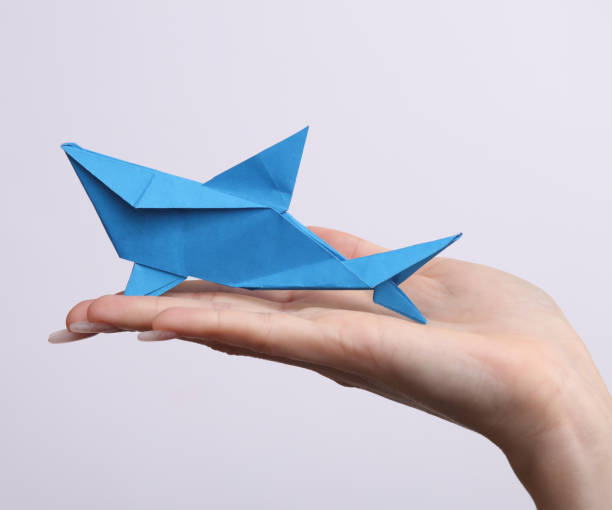 Female hand holds origami shark on white background. Hobby, creativity stock photo