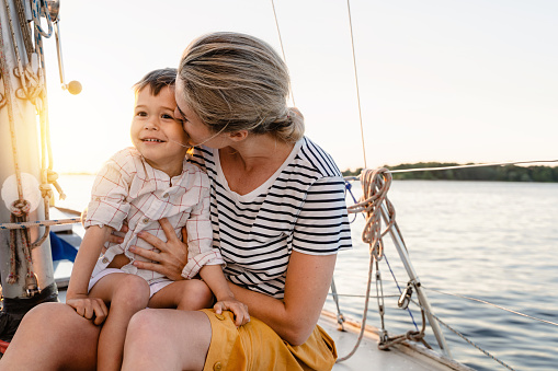 Young attractive mother with her adorable toddler son sailing in sea on sailboat