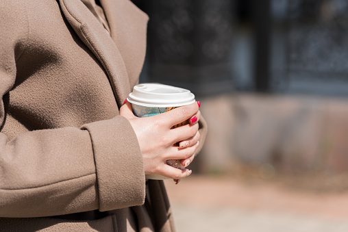 Close-up of a cup of coffee in women's hands on the street.