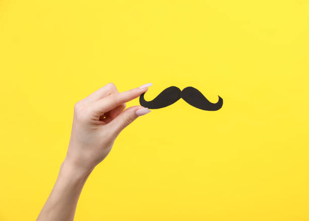 istock Woman's hand holds a mustache cut from paper on a yellow background 1483085306