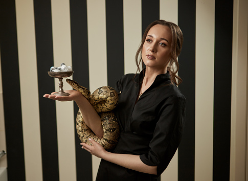 Portrait of beautiful female doctor cosmetologist with snake holding a bowl with medical preparations for injection in the modern clinic. Symbol of medicine