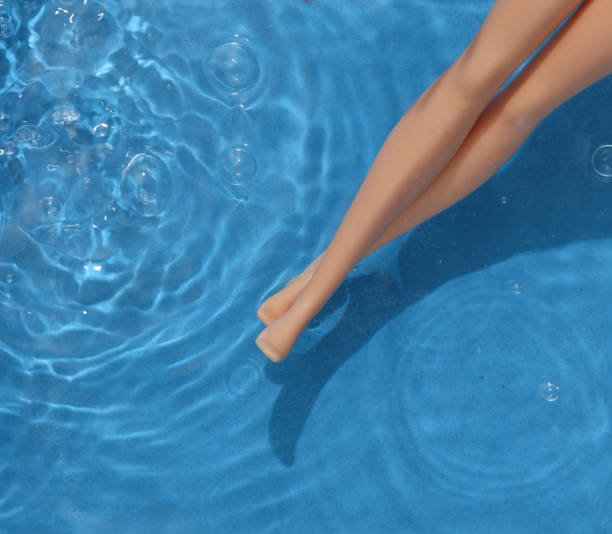 istock Doll legs in blue water with shadows. Beach rest. Top view 1483086048