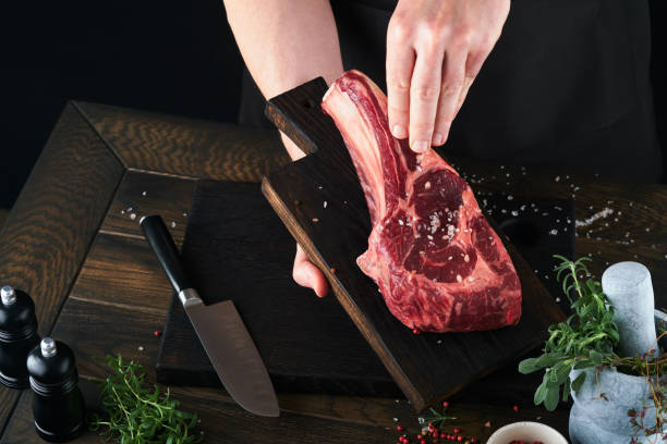 istock Chef cutting steak beef. Mans hands hold raw steak Tomahawk on rustic wooden cutting board on black background. Cooking, recipes and eating concept. Selective focus. 1483090109