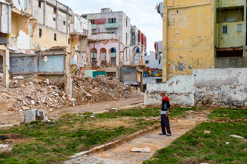 Havana, Cuba - April 14, 2023: A senior man standing on the side of a street staring at a wrecked building. There are other buildings in the background.
