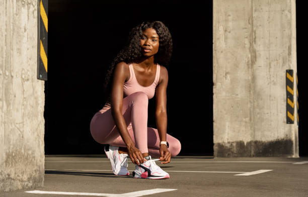 Young African woman runner lacing sneakers before running jogging in urban city.