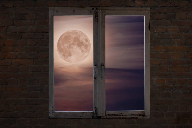 View of the full moon in the clouds through an old window in a brick wall
