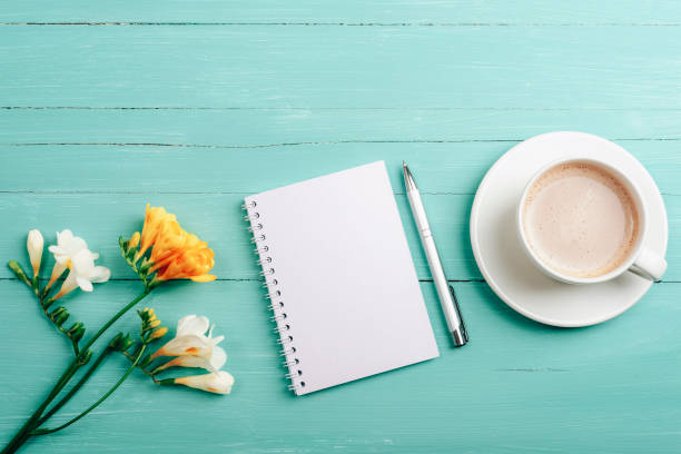 istock Blank notepad, pen and coffee cup on turquoise wooden table with freesia flowers. Top view, flat lay, mockup 1483095293