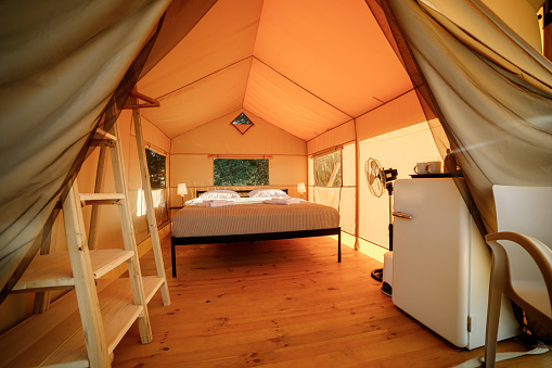 Interior of Cozy open glamping tent with light inside during sunset. Luxury camping tent for outdoor summer holiday and vacation. Lifestyle concept