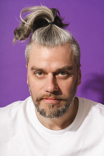 Portrait of middle aged man with funny pony tail against purple background.