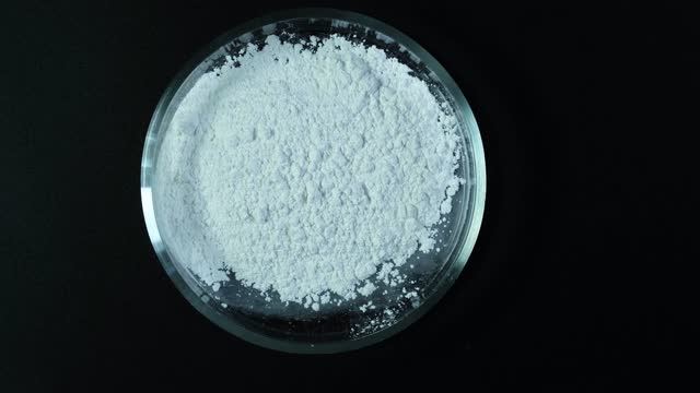 Silicon dioxide powder or Silica. Food additive E551,  anti-caking agent. Silicon oxide. White chemical dust in Petri dish, top view. Video, Rotation motion.