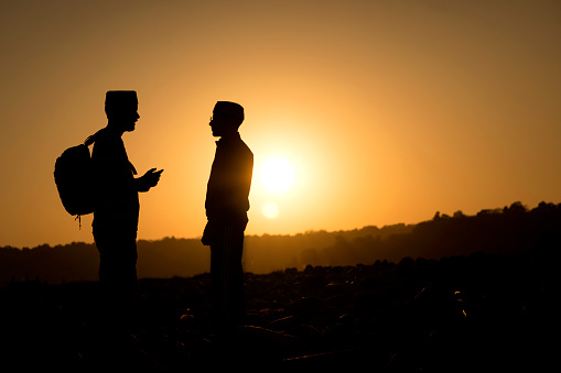 Silhouette image of two Indian young men standing against the beautiful sunset view in the mountains.