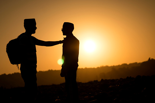 Silhouette image of two Indian young men standing against the beautiful sunset view in the mountains.