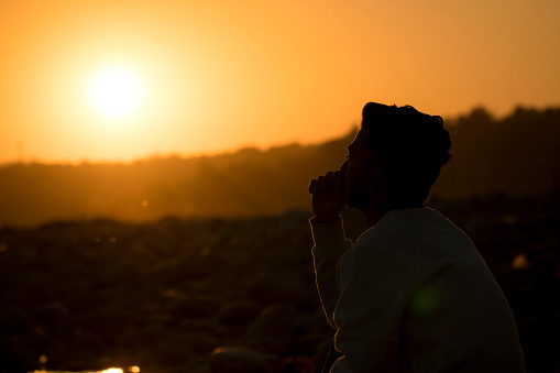 Silhouette portrait of a young man sitting and thinking while enjoying the beautiful sunset view.