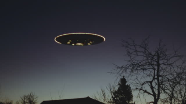 Handheld, grainy footage of UFO, alien flying saucer, flying over houses at dusk. Sci fi movie.