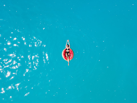 overhead view of woman floating on inflatable ring in blue sea water sunbathing