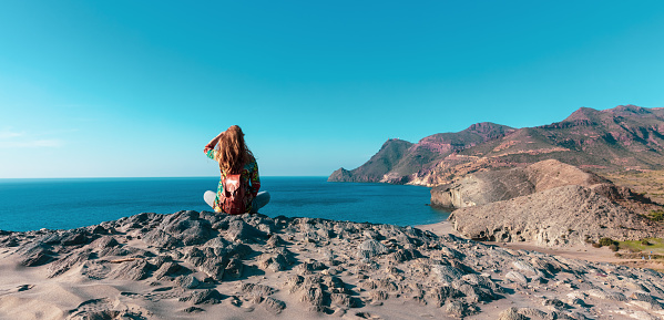 Woman sitting on rock looking at panoramic view of mediterranean sea- Andalusia in Spain