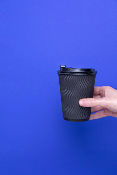 istock Black paper cup with coffee in a female hand on a blue background, copy space 1483111349