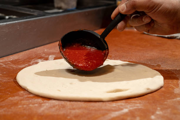 istock Pizzaiolo spreading tomato sauce over an unbaked pizza. 1483112213