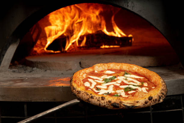 Pizzaiolo pulling a fresh margherita pizza from a hot pizza furnace. Pizza maker pulling a hot, fresh margherita pizza from a hot pizza furnace. wood burning stove stock pictures, royalty-free photos & images