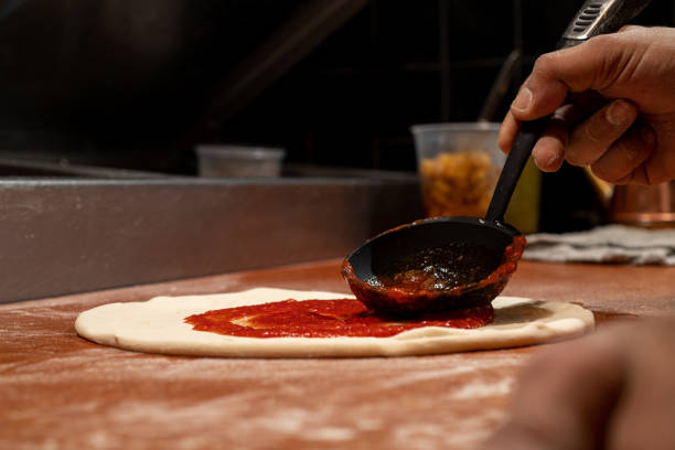 istock Pizzaiolo spreading tomato sauce over an unbaked pizza. 1483112498