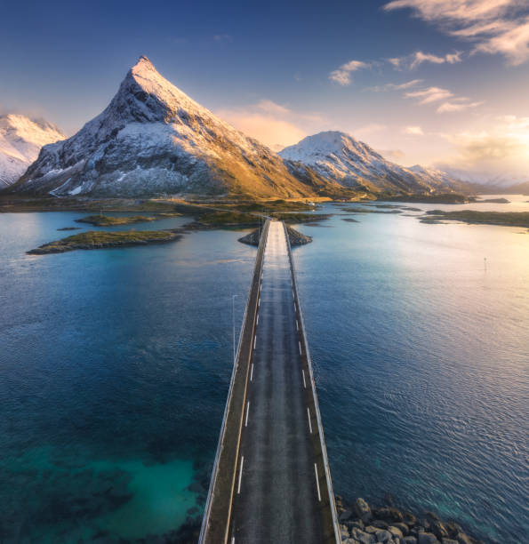 vista aérea del puente sobre el mar y las montañas nevadas en las islas lofoten, noruega. puentes de fredvang al atardecer en invierno. paisaje con agua azul, rocas en la nieve, carretera, cielo con nubes. vista superior del dron - above the cloud sea fotografías e imágenes de stock