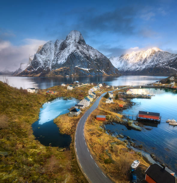 vista aérea de la isla con rorbu, mar, puente, hierba naranja, montañas nevadas, cielo azul con nubes al amanecer en primavera. hermoso paisaje. vista superior del dron. reine village, islas lofoten, noruega - above the cloud sea fotografías e imágenes de stock