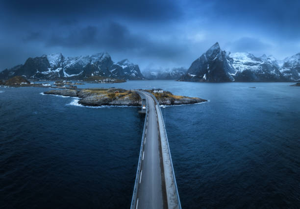 vista aérea del puente, isla con rorbu, mar, montañas nevadas en niebla, cielo azul nublado en el crepúsculo en primavera. paisaje espectacular. vista superior del dron de la carretera. hamnoy village, islas lofoten, noruega - above the cloud sea fotografías e imágenes de stock