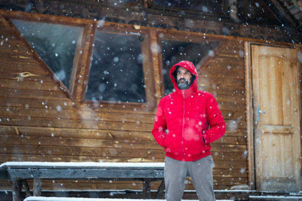 istock Cabin getaway. Man enjoying snowfall from log cabin. 1483117168