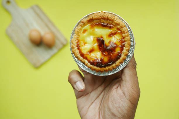 istock holding a a egg tart against yellow background 1483117310